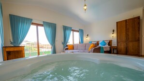 A room with a large bathtub, a sofa with colorful cushions, and a wooden wardrobe. - Ada Villa (Fethiye)