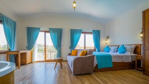 A spacious bedroom with a large bed, a wooden floor, and a view of the outdoors through the windows. - Ada Villa (Fethiye)