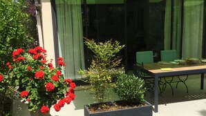 Een patio met een tafel en stoelen, omringd door potplanten en een raam met gordijnen.