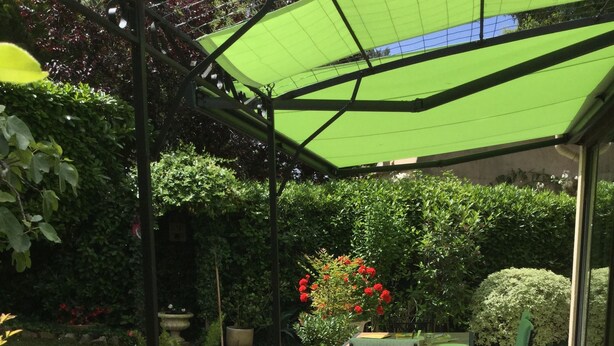 Een terras met een tafel en stoelen, omringd door groen en een pergola met een groen dak.