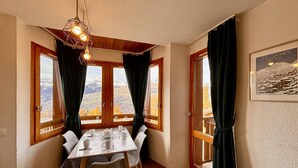 Un comedor con una mesa dispuesta para cuatro, ventanas amplias con cortinas y vistas a la montaña.