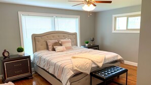 A bedroom with a bed, bedside tables, a bench, a ceiling fan, and large windows. - The Grand Gorge Villa-With Yard& Parking (Niagara Falls)