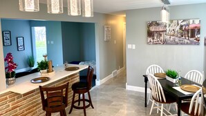 A modern kitchen with a brick backsplash, pendant lights, and a dining area with white chairs and a black table. - The Grand Gorge Villa-With Yard& Parking (Niagara Falls)