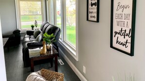 A living room with a black leather sofa, a coffee table with decorative items, and two framed inspirational quotes on the wall. - The Grand Gorge Villa-With Yard& Parking (Niagara Falls)