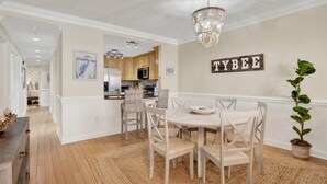 A dining area with a round table, white chairs, a chandelier, and a potted plant. - Great Family Condo with Pool Views! Pool Access (Tybee Island)