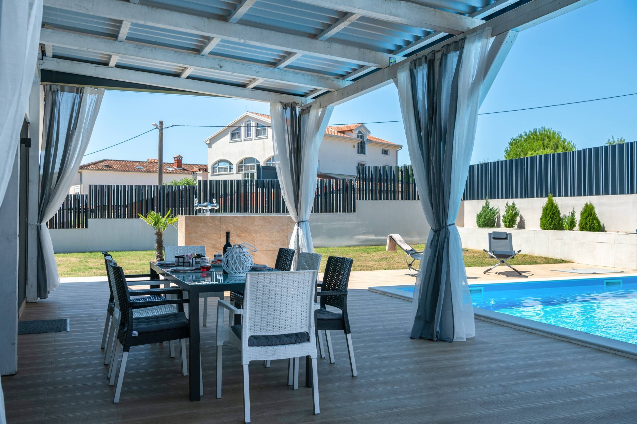 En udendørs terrasse med pool, spisebord og stole.