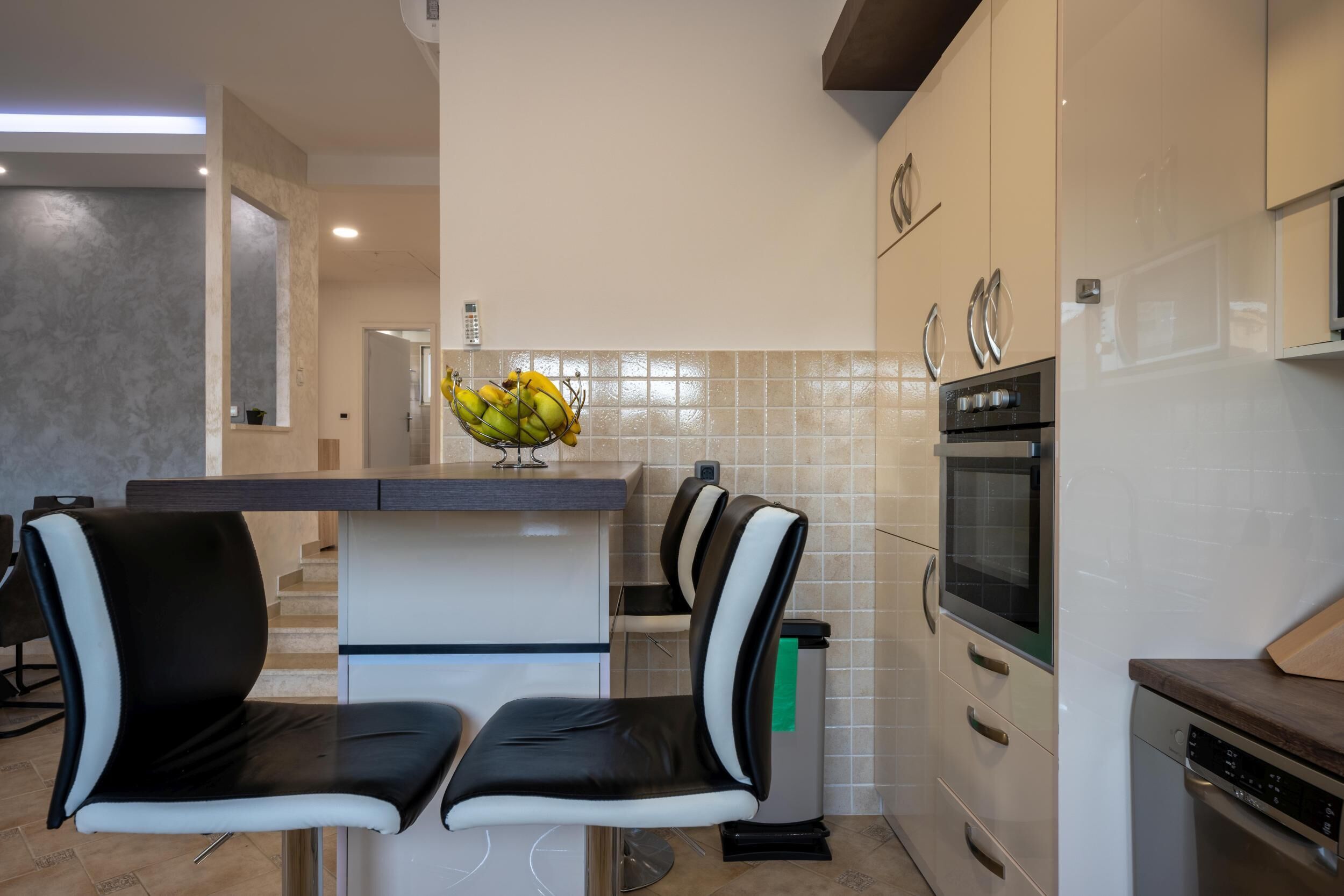 Una cucina moderna con due sedie bianco e nero, una ciotola di frutta, un forno a microonde e una lavastoviglie.