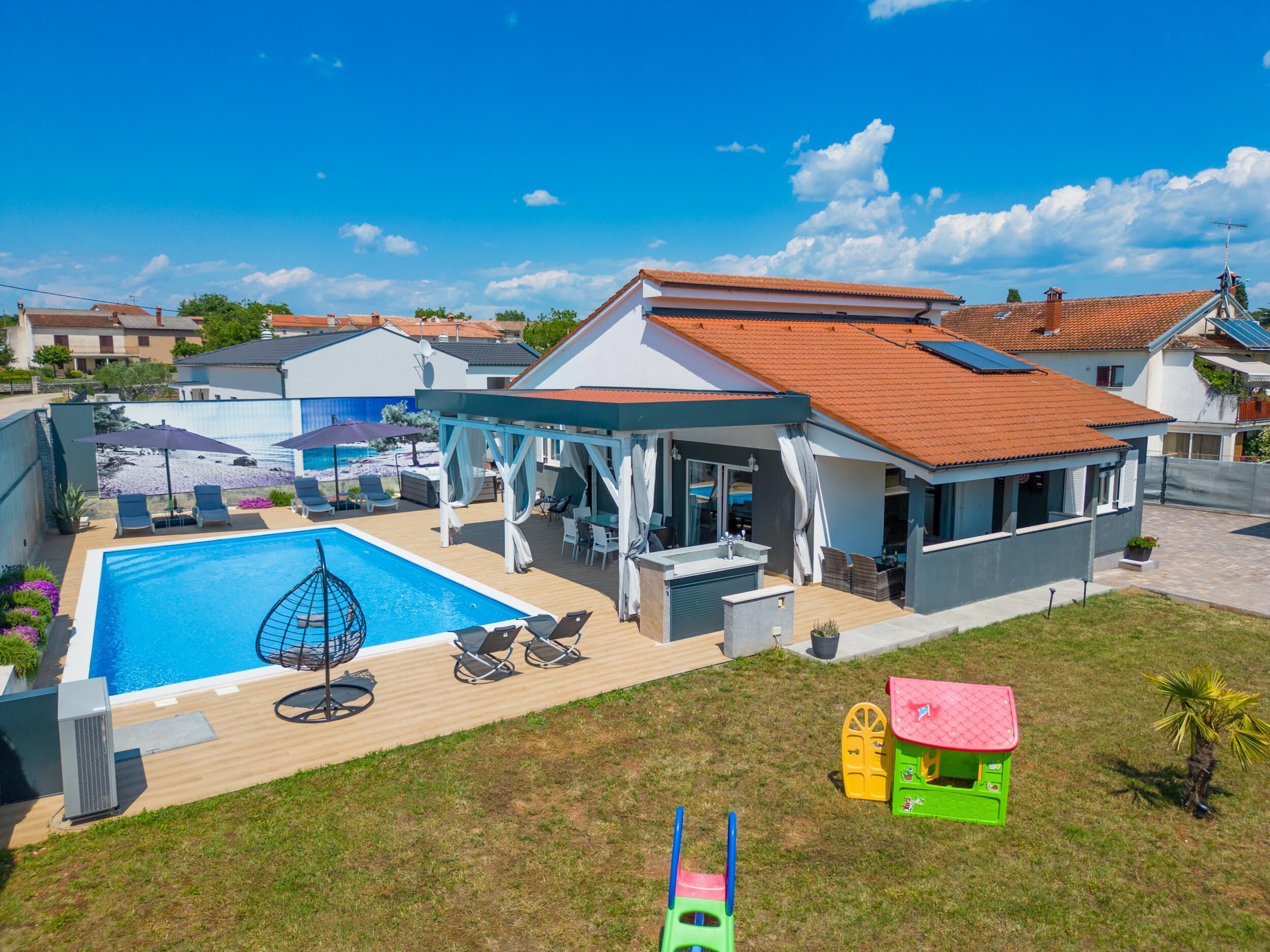A residential property with a swimming pool, outdoor seating, and a covered patio area.