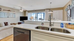 A modern kitchen with a dishwasher, double sink, and a dining area with a TV. - Ocean Views, Heated Pool Access, Steps to Beach (Tybee Island)