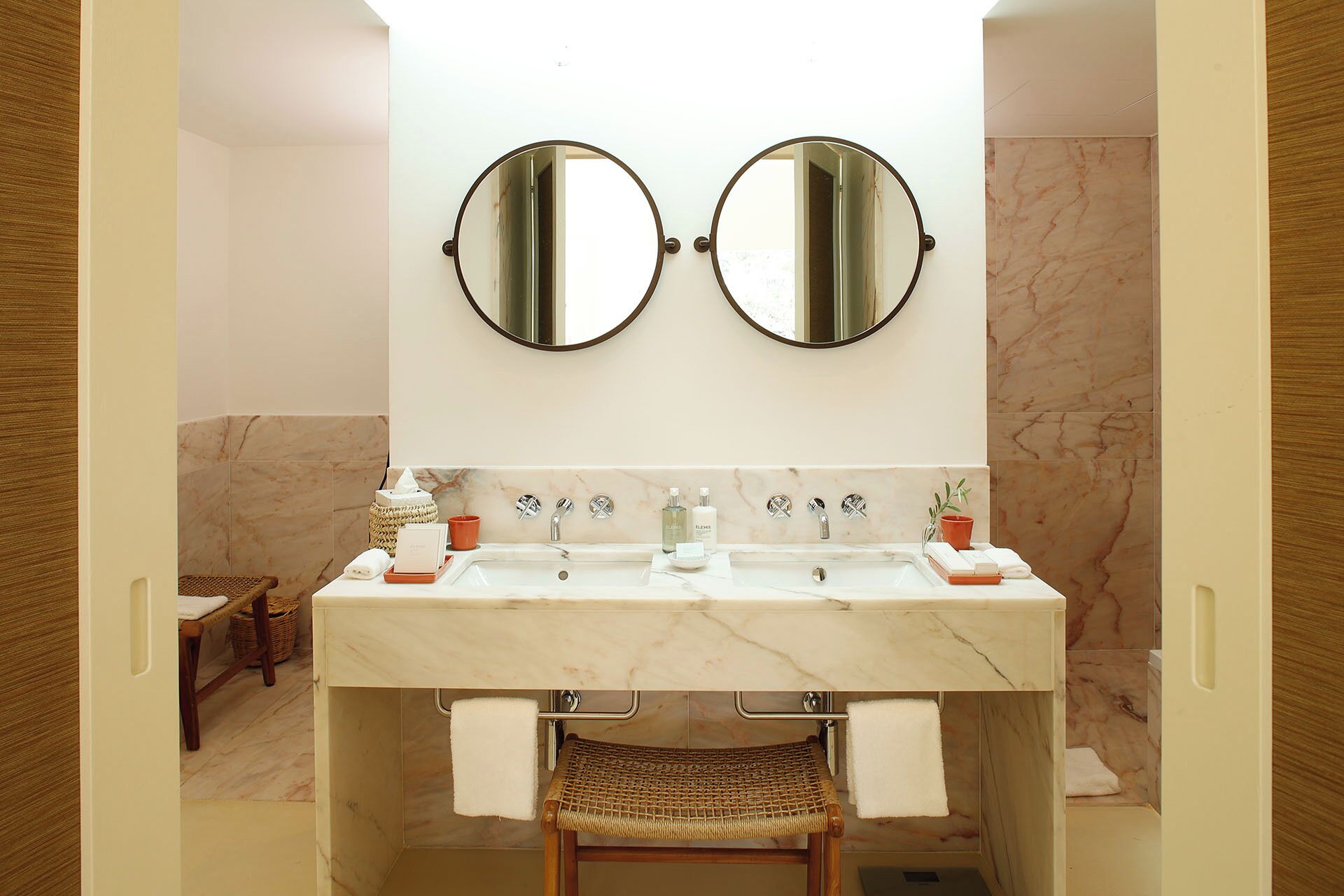 Une salle de bain avec deux miroirs, un lavabo et une chaise en osier.