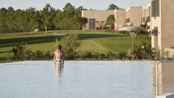 Eine Frau in einem Badeanzug in einem großen, klaren Pool mit Blick auf einen Golfplatz und moderne Gebäude im Hintergrund.