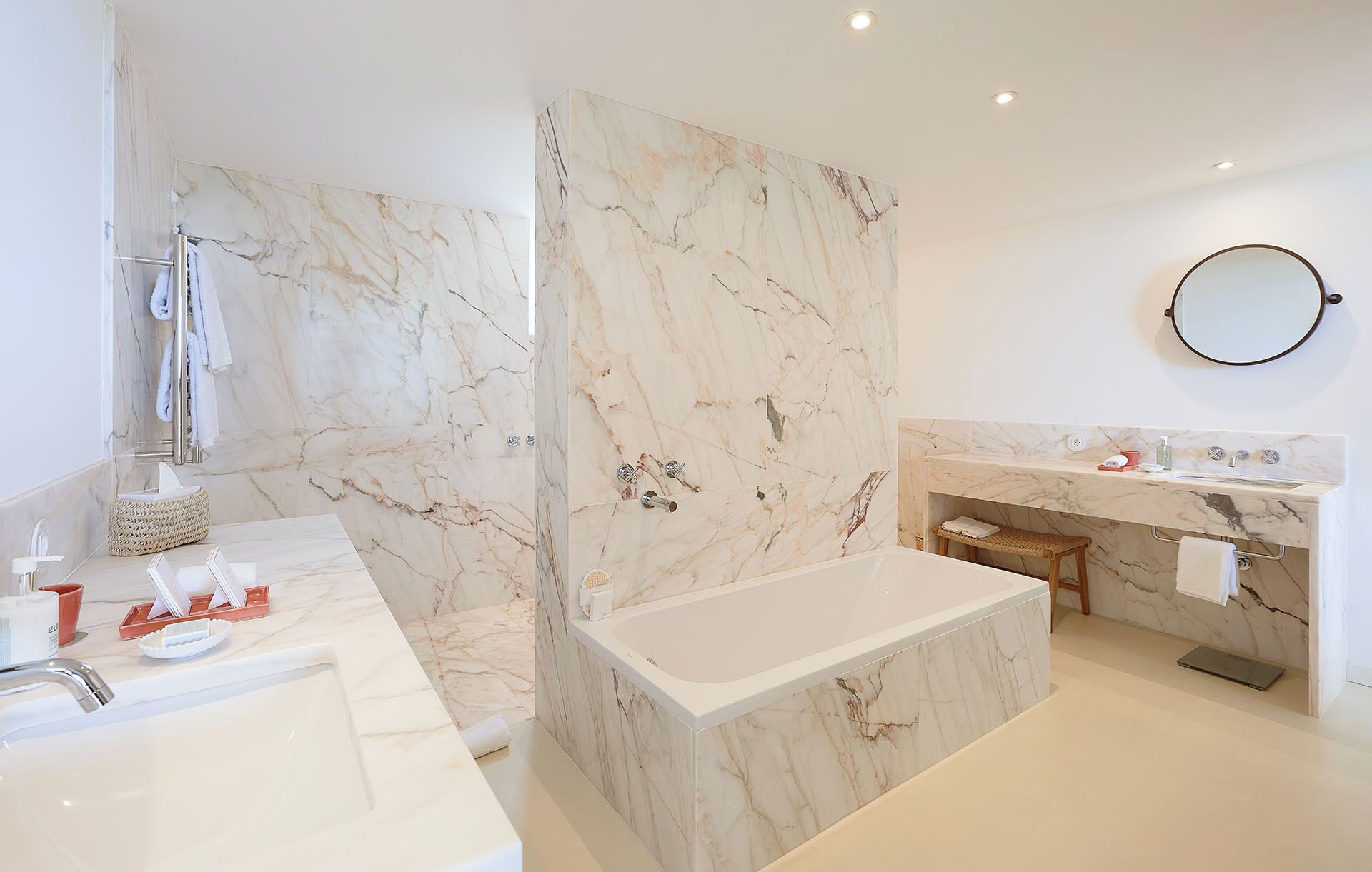 A modern bathroom with a marble shower, a bathtub, a vanity with a sink, and a round mirror.