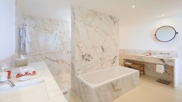 A modern bathroom with a marble shower, a bathtub, a vanity with a sink, and a round mirror.