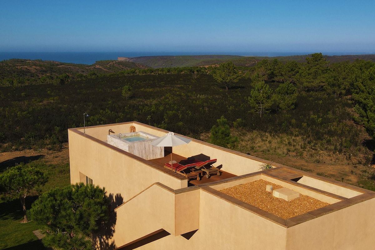 A rooftop terrace with a hot tub, seating area, and a view of the surrounding landscape.