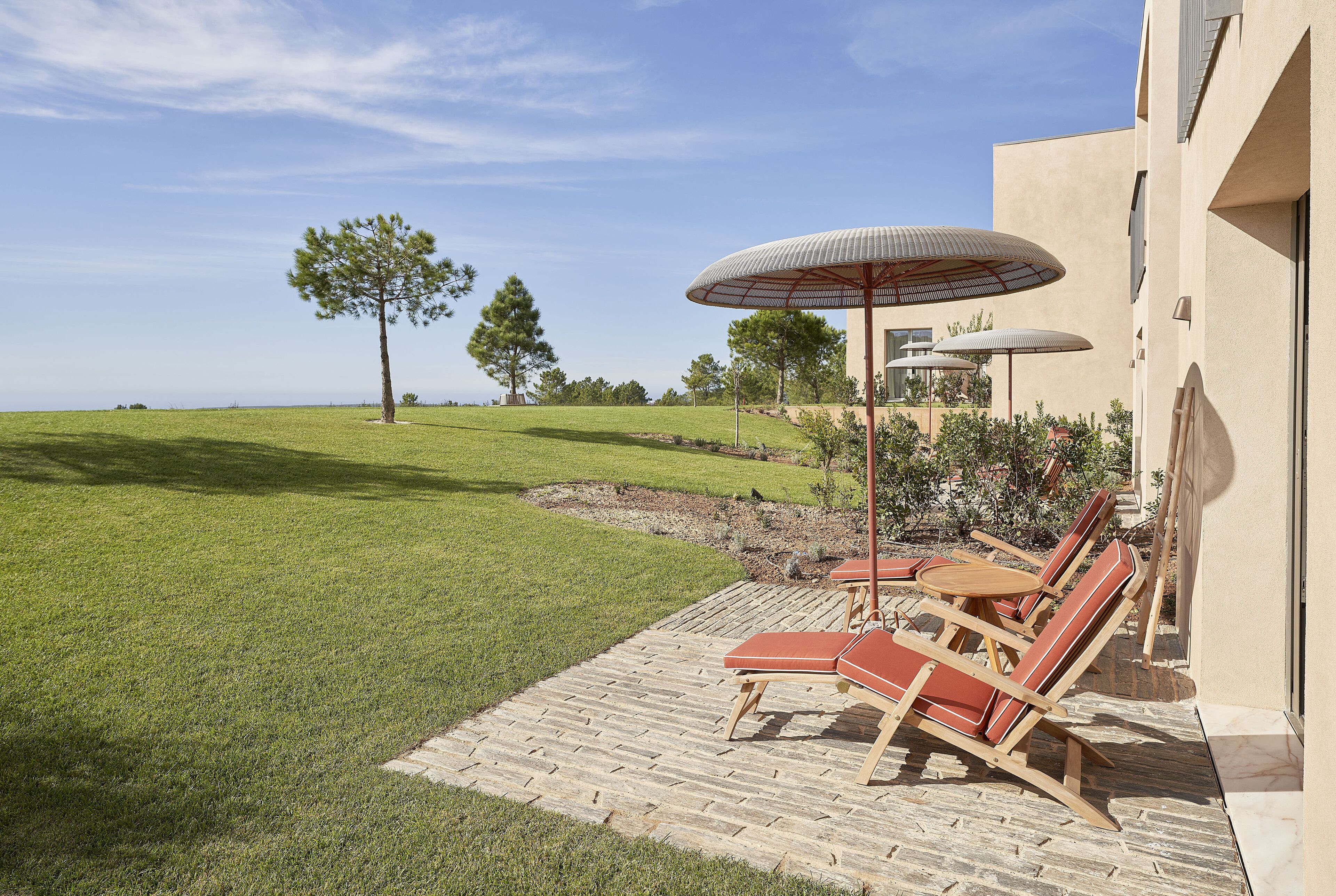 A patio with lounge chairs and umbrellas, a grassy lawn, and a building with a modern design.