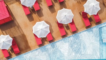Vista aérea de una zona de piscina con múltiples sillones rojos y sombrillas blancas.