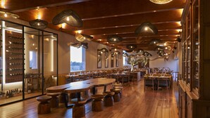Un ristorante con tavoli e sedie in legno, luci a sospensione e una cantina per il vino.