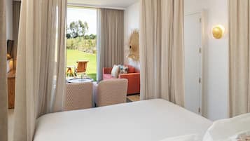 A hotel room with a large bed, a red sofa, two patterned armchairs, and a view of an outdoor garden area through a glass door.