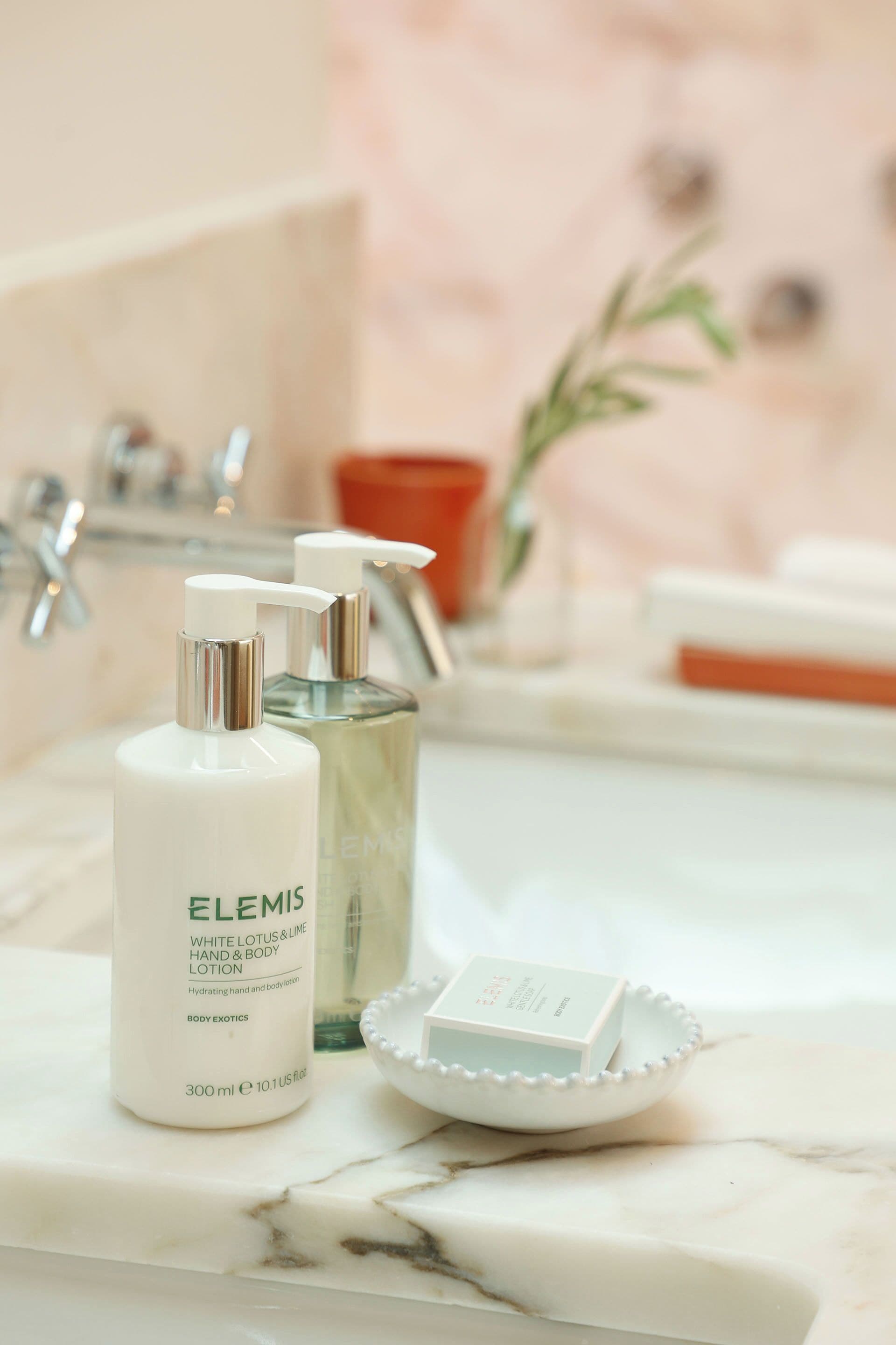 A bathroom with a marble countertop, a white bottle of Elemis lotion, and a glass bottle.