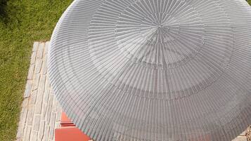 Une table ronde surmontée d’un parasol à motifs, entourée de chaises rouges à coussins, le tout posé sur une terrasse en pierre.