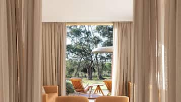 A hotel room with a large bed, beige curtains, and a view of an outdoor seating area with chairs and a table.