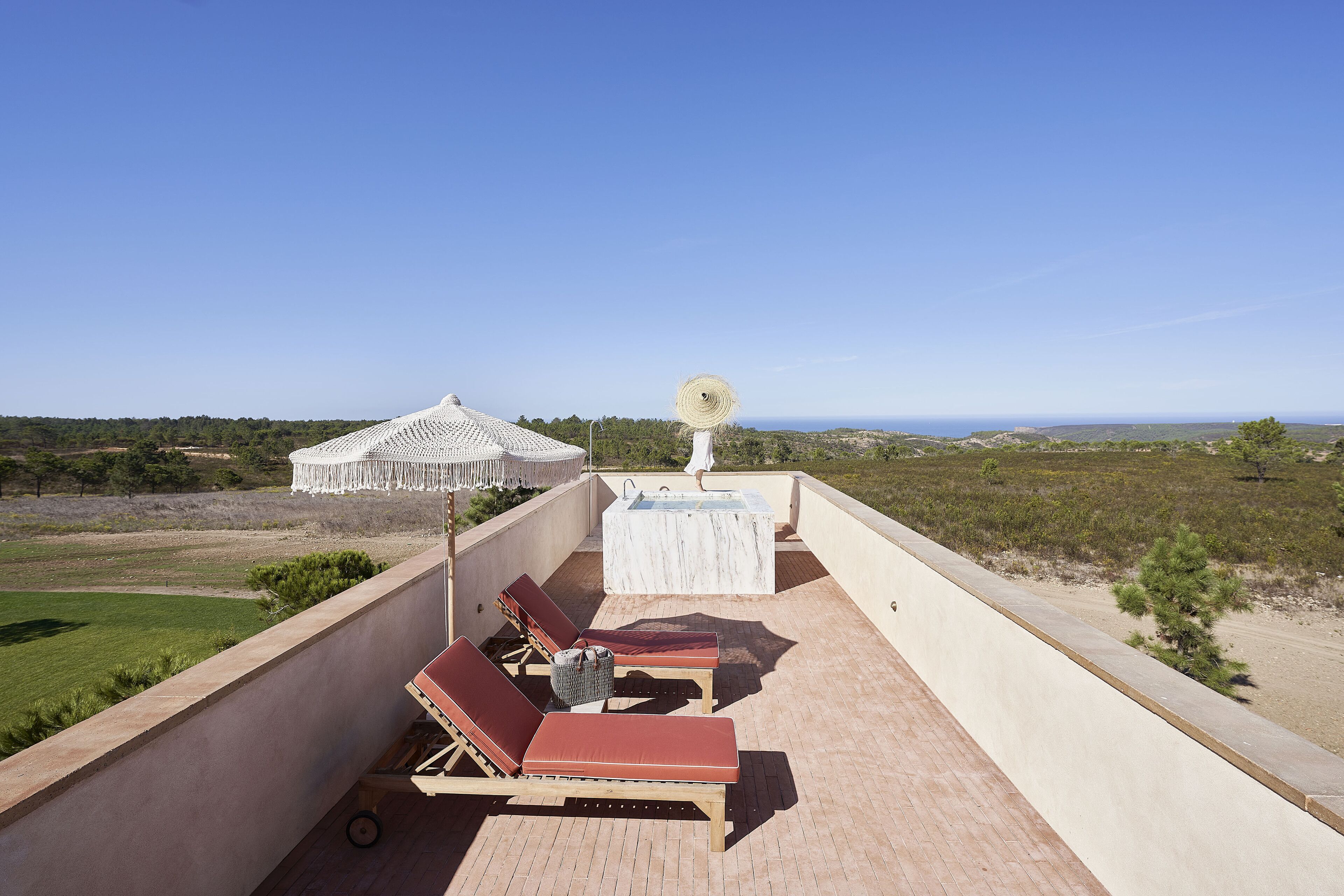 A rooftop terrace with lounge chairs, a hot tub, and a view of the landscape.