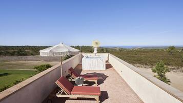 A rooftop terrace with lounge chairs, a hot tub, and a view of the landscape.