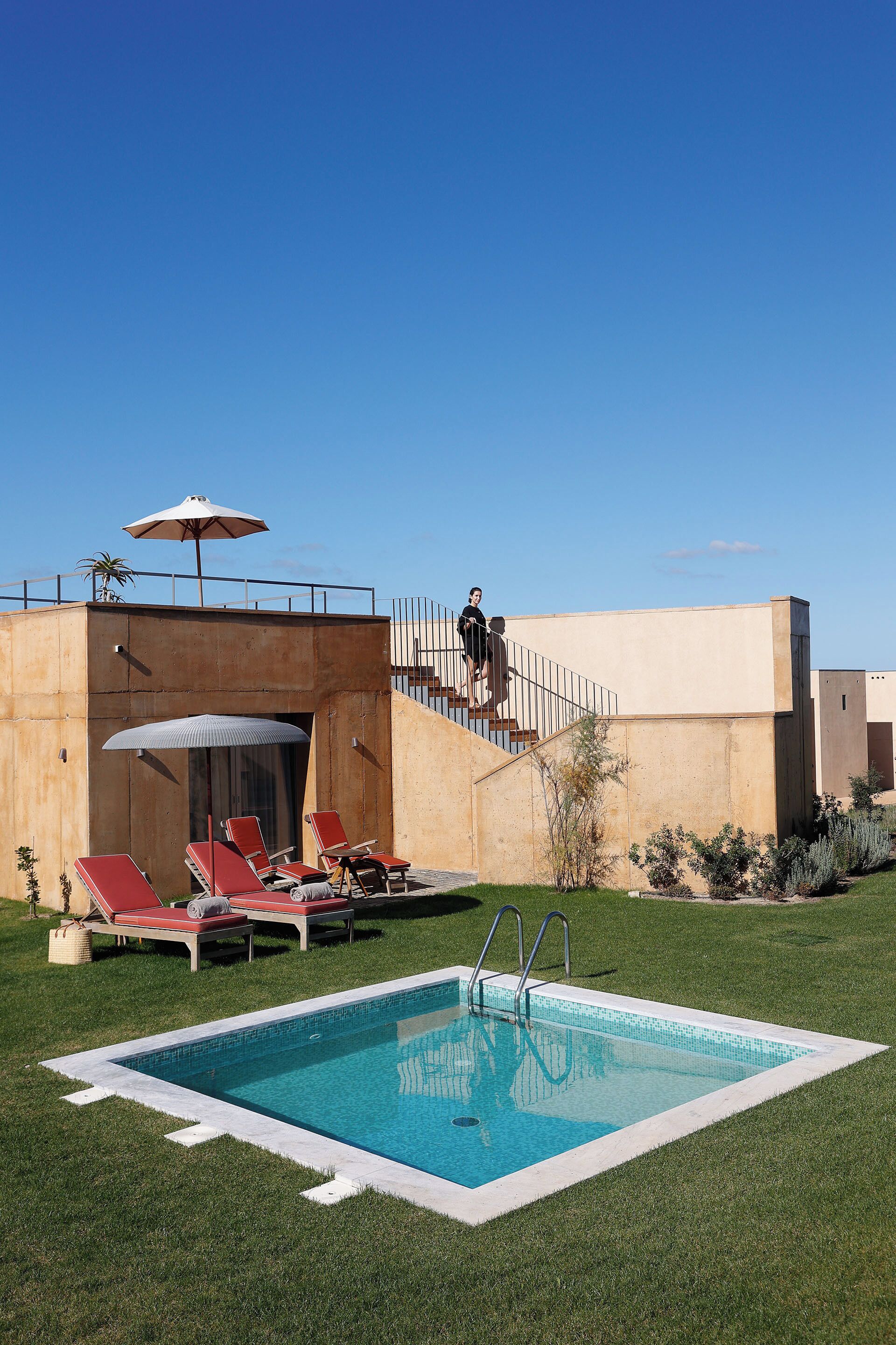 Una piscina con sillas de descanso rojas y una persona subiendo escaleras.