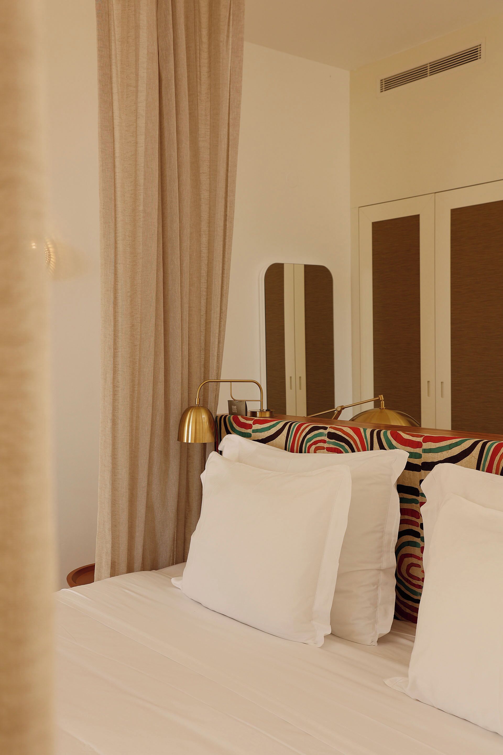A hotel room with a bed, a bedside lamp, a mirror, and a wardrobe.