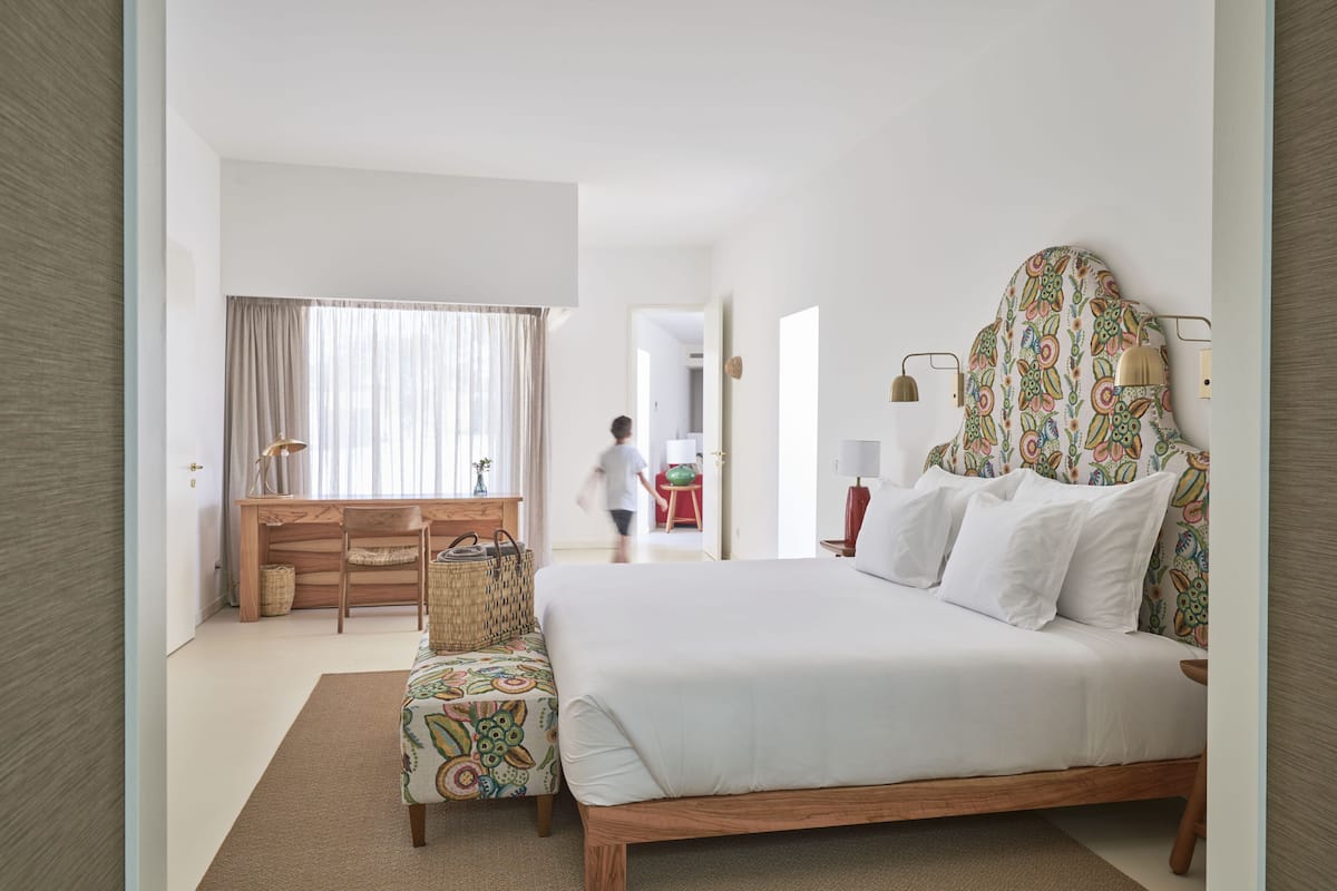 A bedroom with a large bed, a desk, a chair, and a window with curtains.