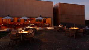 Zona pranzo all'aperto con tavoli, sedie e ombrelloni, con un edificio sullo sfondo.