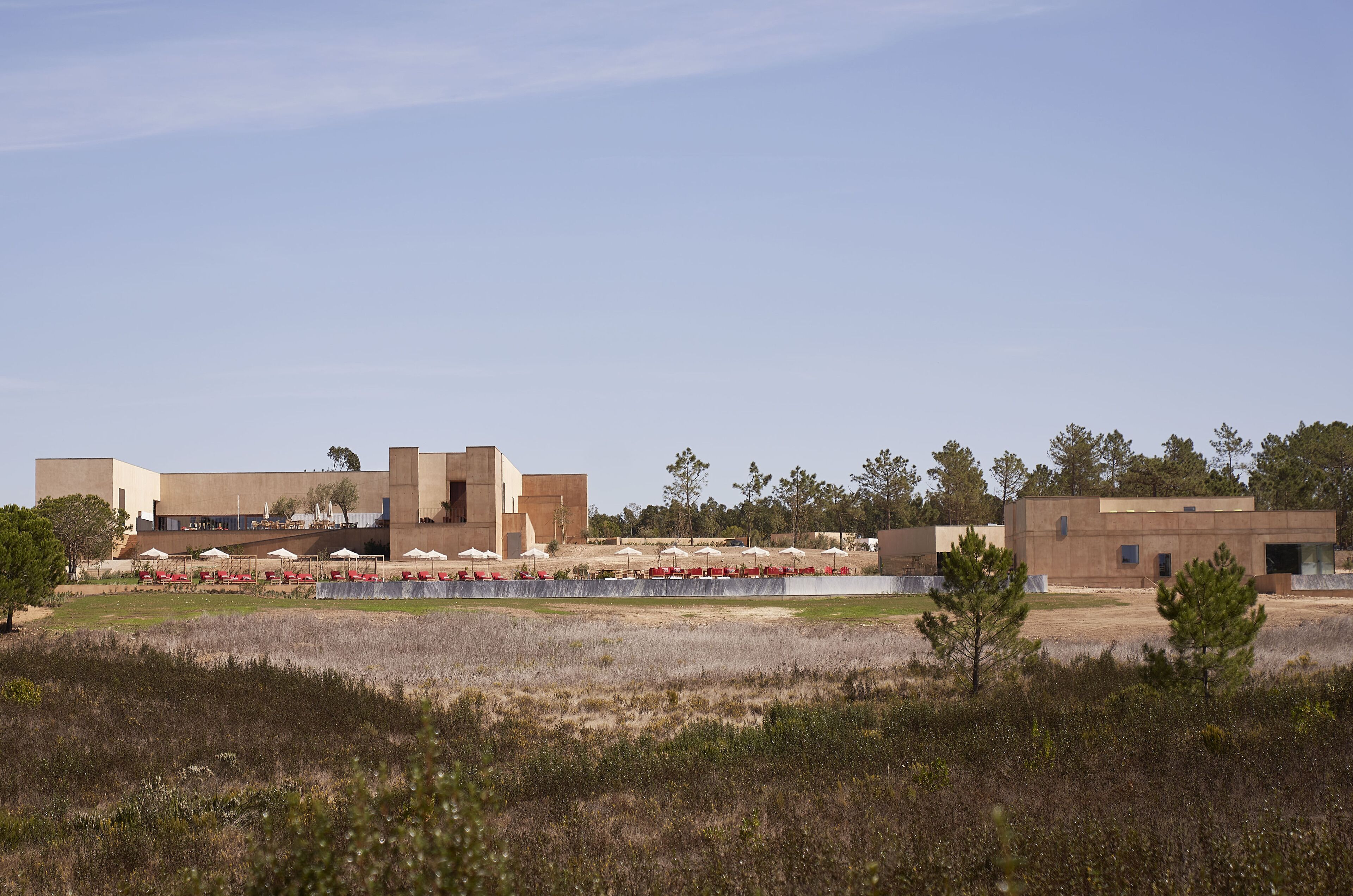 A modern building complex with multiple structures, a landscaped area with trees, and a clear sky.