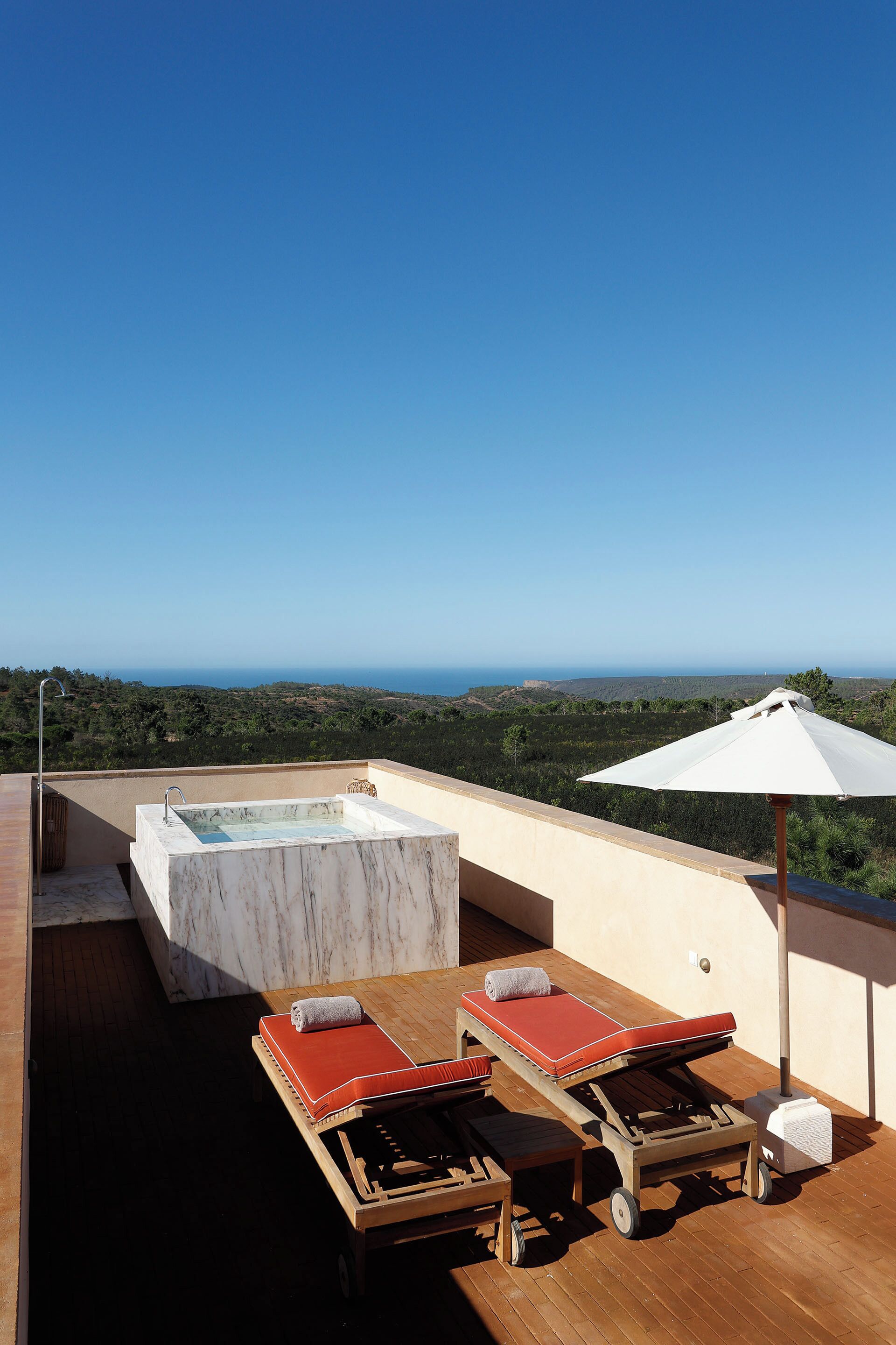 A rooftop terrace with a hot tub, two lounge chairs, and a table with a canopy.