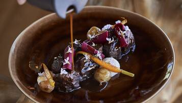 Une main verse de la sauce sur un plat contenant de la viande et des légumes.