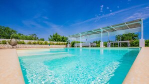 A clear blue pool with a covered seating area and stone walls.
