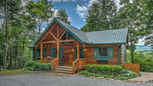 A log cabin with a porch, surrounded by trees and a view of the landscape. - Poppy's Place - Mountain View | Hot Tub | Fire Pit | Shuffleboard | Ping Pong (Ellijay)