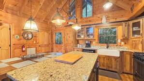 A wooden cabin with a kitchen featuring granite countertops, wooden cabinets, and pendant lighting. - Poppy's Place - Mountain View | Hot Tub | Fire Pit | Shuffleboard | Ping Pong (Ellijay)