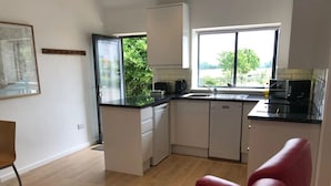 A compact kitchen with a window, a red leather sofa, and a dining area. - The Dairy - Spectacular views, country walks, cozy nights, pet friendly. (Robertsbridge)