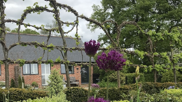 A garden with a brick house, green hedges, and flowering plants. - The Dairy - Spectacular views, country walks, cozy nights, pet friendly. (Robertsbridge)