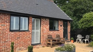 A brick house with a sloped roof, a wooden bench, and two white chairs in the garden. - The Dairy - Spectacular views, country walks, cozy nights, pet friendly. (Robertsbridge)