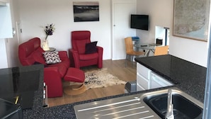 A compact living space with a kitchenette, a red sofa, a dining area, and a flat-screen TV mounted on the wall. - The Dairy - Spectacular views, country walks, cozy nights, pet friendly. (Robertsbridge)