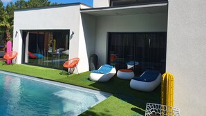 A modern outdoor pool area with a glass-enclosed patio, lounge chairs, and a cactus plant. - Architect-designed villa with heated pool (Moliets et Maa)