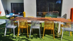 An outdoor dining area with a wooden table and chairs, surrounded by artificial grass and a pool. - Architect-designed villa with heated pool (Moliets et Maa)