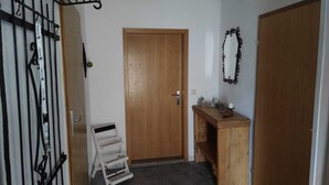 Un couloir avec une porte en bois, une petite table en bois sur laquelle est posé un panneau indiquant « BIENVENUE », et un portail en métal.