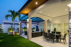 An outdoor patio with a dining area, stone pillars, and a glass ceiling. - Orchid Paradise Homes OPV510 (Hua Hin)