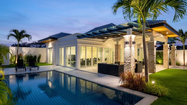 Ein modernes Haus mit Swimmingpool, überdachter Terrasse und gepflegtem Rasen.