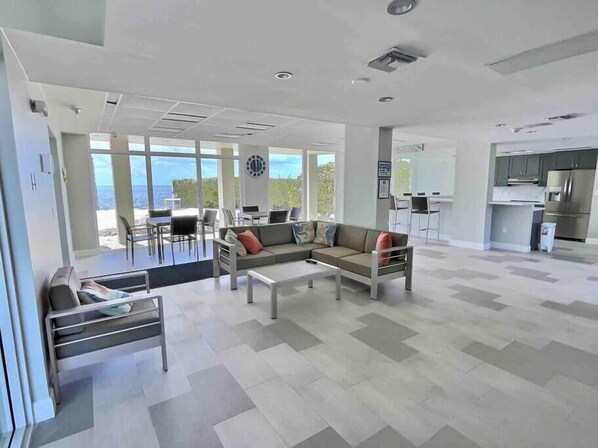A spacious living area with a sofa, coffee table, and dining table. There is a kitchen area with modern appliances and a view of the ocean.