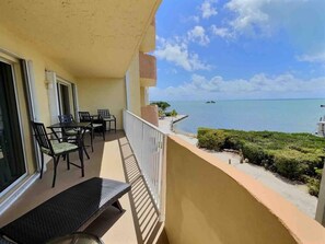 Un balcon avec une table et des chaises, donnant sur une plage et l’océan.