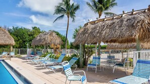 Un espace aménagé au bord de la piscine, avec des chaises longues, une piscine et des parasols en chaume.