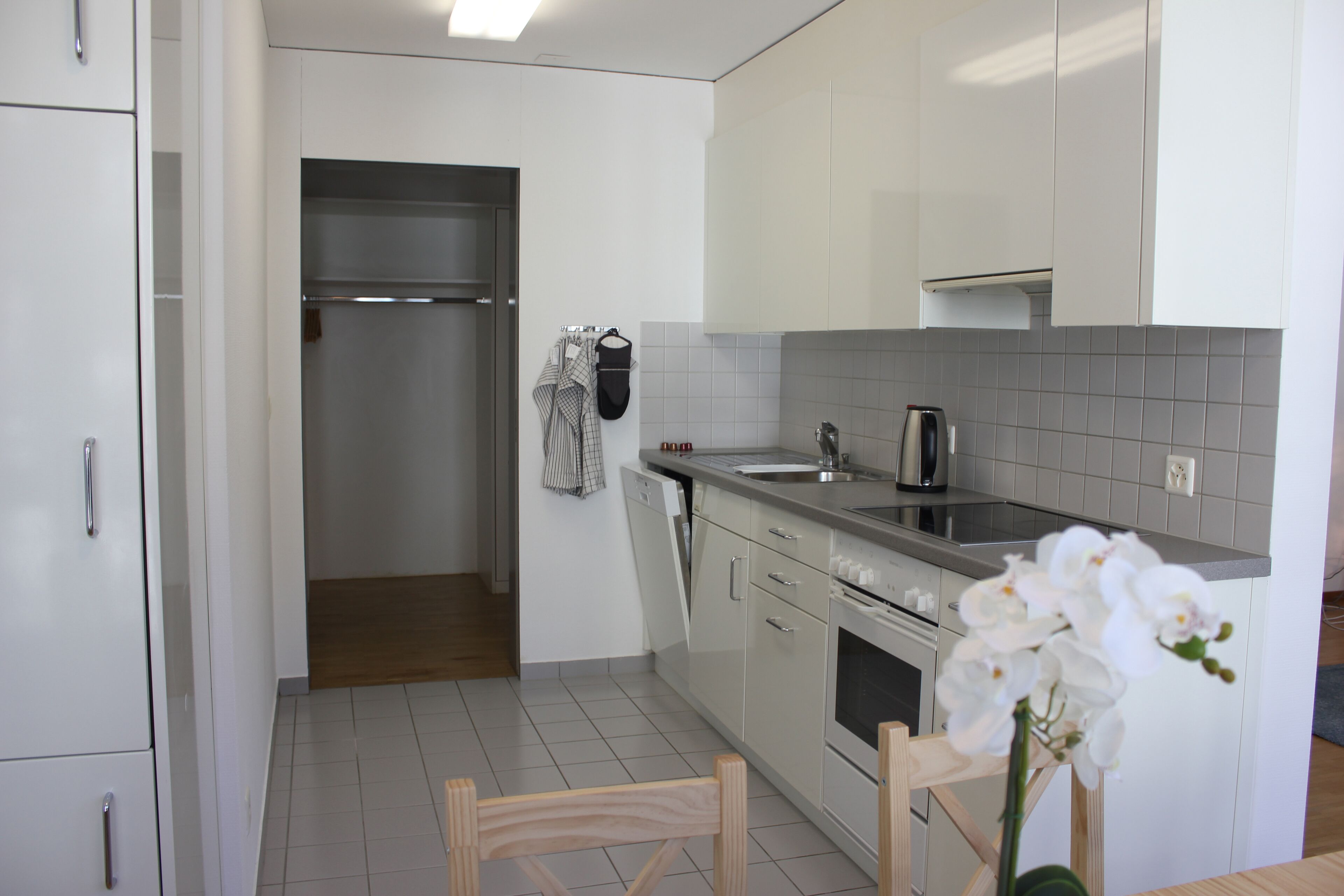 A modern kitchen with white cabinets, a stainless steel countertop, and a built-in oven.